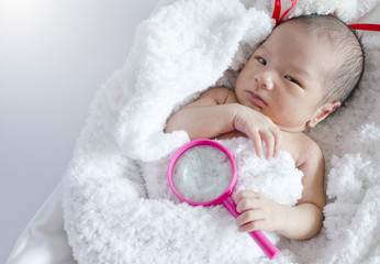 Newborn baby wrapped in a blanket in the basket with Magnifying glass, look at camera