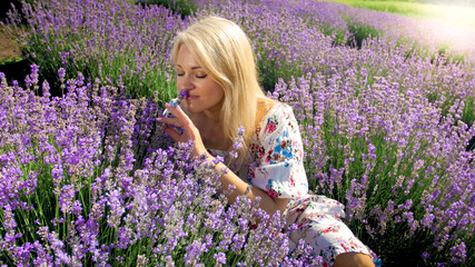 Closeup portrait of young blonde woman smelling lavender flowers in field