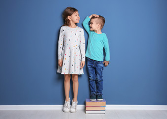 Little girl and boy measuring their height near color wall
