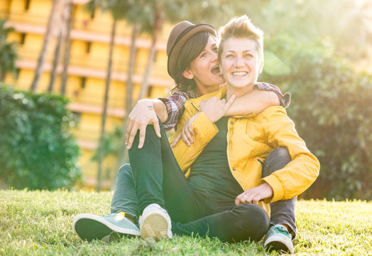 Happy girlfriends in love sharing time together at travel trip hugging at garden - Playful women friendship concept with girls couple having fun on fashion clothes outdoors - Bright warm sunset filter