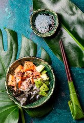 Hawaiian salmon poce with avocado, rice and sesamo served in bowls on tropical leaves. Turquoise...