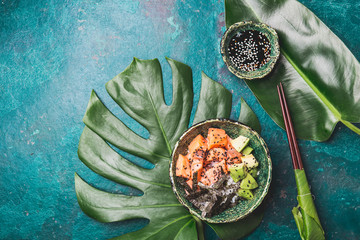 Hawaiian salmon poce with avocado, rice and sesamo served in bowls on tropical leaves. Turquoise...