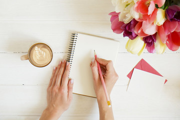 Overhead shot of woman hands drawing, writing with pencil in open notebook, drinking coffee on...