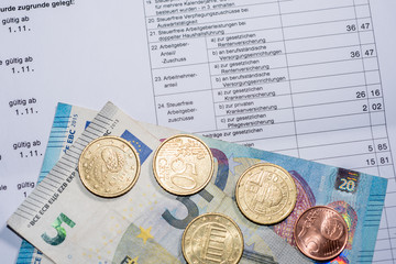 Ausschnitt einer Gehaltsabrechnung mit Münzen und Euroscheinen