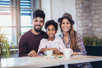 Mom and dad drawing with their daughter. Girl and mixed race parents having fun at home.