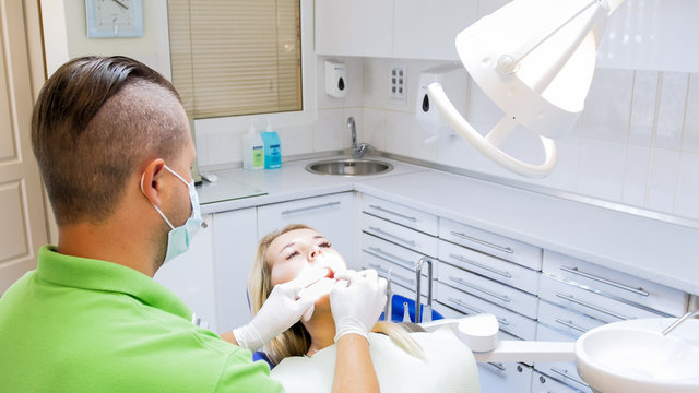Closeup image of dentist in protective gloves inspecting woman teeth