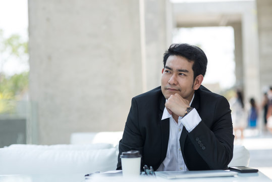 Thoughtful Asian businessman sitting in cafe with city background.