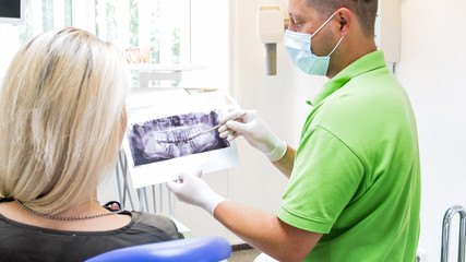 Male orthodontist talking to his patient and showing x-ray of teeth