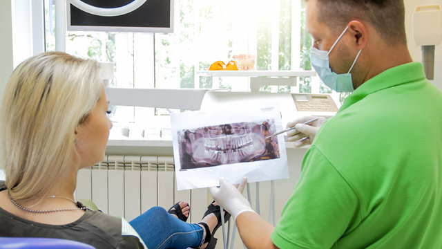 Closeup photo of doctor talking about teeth treatment and showing x-ray image to his patient
