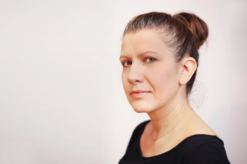 Fototapeta premium Sad middle-aged woman on a gray background. She is sad because she has gray hair