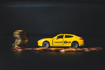 Closeup yellow taxi with golden stack coins on dark background