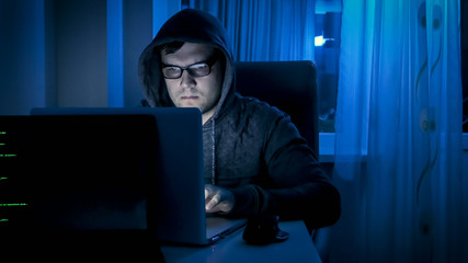 Young concentrated man in eyeglasses working on laptop at night