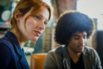 Woman listening to colleague or client,afro american man in background.Group of multiethnic people having business team meeting in restaurant lounge.Teamwork,corporate,diversity and social concepts.
