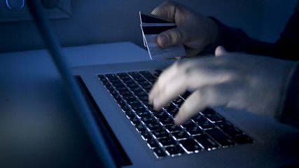 Closeup image of person holding credit cards typing on computer keyboard. Concept of e-commerce and...