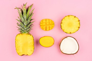 Tropical fruit flat lay with pineapple, mango, and coconut on a pastel pink background