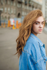street portrait of a young attractive emotional girl with curly slips dressed in a trendy blue denim suit on a style strolling outdoors. look at the camera