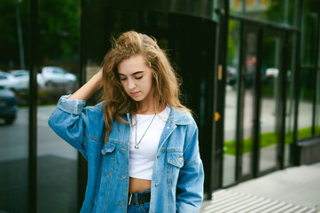 street portrait of a young attractive emotional girl with curly slips dressed in a trendy blue jeans suit on a style walking in the open air