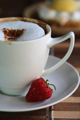 A cup of hot coffee with strawberry on white saucer.