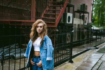 Obraz na płótnie Canvas street portrait of a young attractive emotional girl with curly slips dressed in a trendy blue jeans suit on a style walking in the open air