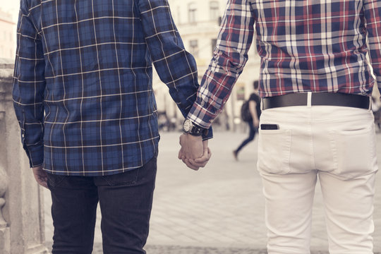 rear capture of a young cheerful gay couple in plaid shirts walking in the street of a southern bohemian city