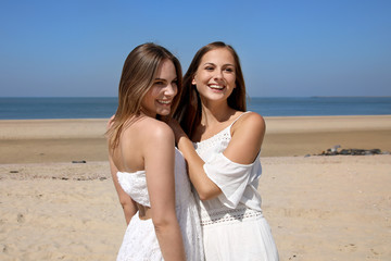 Zwei hübsche blonde Frauen umarmen sich am Strand und lachen