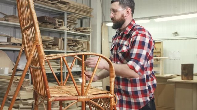 carpenter in checkered shirt with a beard in the workshop examines a rocking chair
