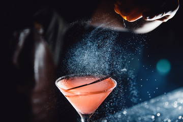 Large cocktail in martini glass with droplets of spray is prepared by barman.