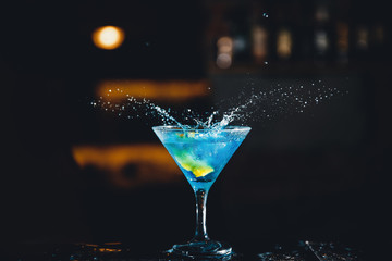 Large cocktail in martini glass with droplets of spray is prepared by barman.