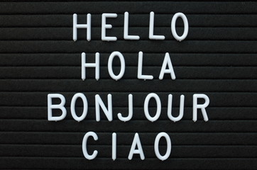 The words Hello, Hola, Bonjour and Ciao in white plastic letters on a black letter board as a friendly greeting from Europe