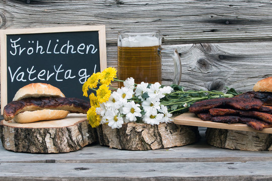 Text "Fr&ouml;hlichen Vatertag" mit Bratwurst und Bauchfleisch  und Bier rustikal auf Holz