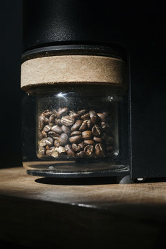 Coffee Beans in Glass Grinder Jar with Dark Background and Warm Light