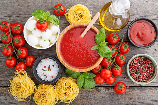 Ingredients For Cooking - Tomato Sauce, Pasta, Tomatoes, Garlic, Olive Oil On The Old Wooden Background. Top View.