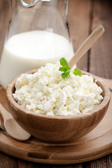 Homemade cottage cheese in a wooden bowl on dark wooden background. 