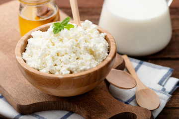 Homemade cottage cheese in a wooden bowl on dark wooden background. 
