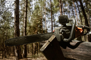 Profile view photo of a chainsaw laying on a wood log on forest background.