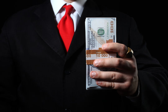 Photo of a rich businessman in black siut with red tie holding a money pack.