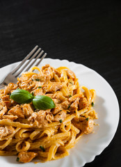 Sliced fried chicken breast meat in a creamy sauce with bavette pasta in a plate on wooden table