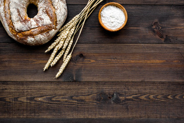 Home bread with classic recipe. Round loaf near ears of wheat on dark wooden background top view copy space