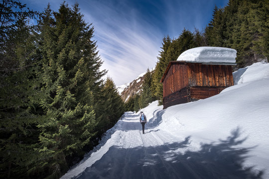 Winterspaziergang an einer Bergh&uuml;tte mit viel Schnee auf dem Dach vorbei