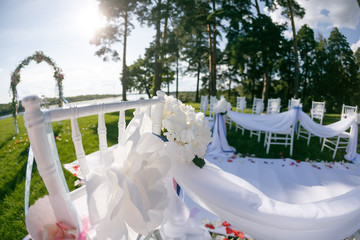 tapes fly in the wind. Romantic wedding ceremony. White wooden chairs with ribbon and flowers on a green lawn. Nice armchairs for guests