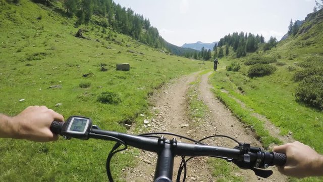 POV man riding e-bike following friend woman.Mtb action cyclist exploring together mountain trail path.Electrical bike active people sport travel vacation in Italy Alps outdoors in summer.4k video