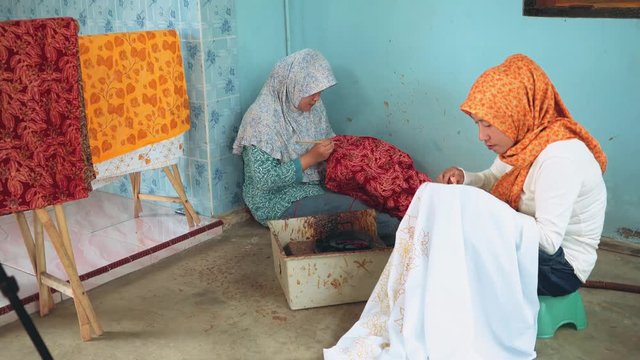 Two adult indonesian women painting batik with canting