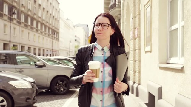 Business woman with dark hair, glasses, coffee and documents, goes to the business center confident gait, in slow motion