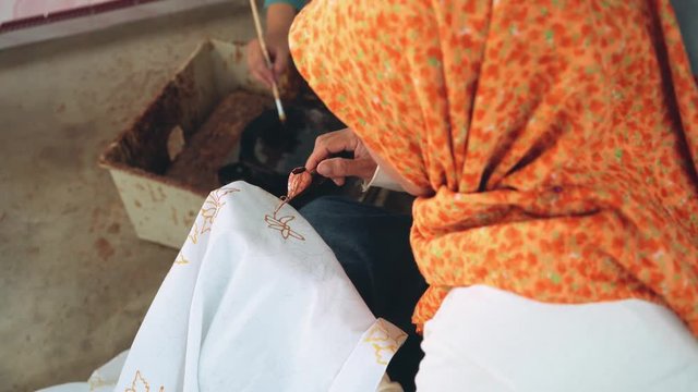Adult indonesian woman painting batik with wax using canting