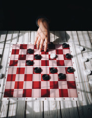 Children's hands on a checkerboard. The caucasian child plays checkers. Play board games. Loss,...