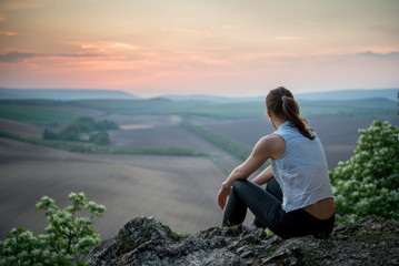 sporty girl sitting on high rock and enjoy the sunset