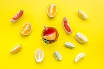 Concept of alcoholic cocktail with fruits. Glass with beverage near oranges, grapefruit, lime and rosemary on yellow background top view pattern