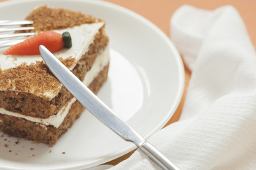 Slice of home made carrot cake with carrot decorations on white plate close-up, napkin, knife, selective focus