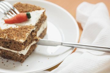 Slice of home made carrot cake, white plate, napkin. Knife cuts an appetizing piece. Sweet healthy vegan food. Selective focus, copy space