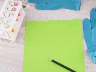 record diagnosis, medical report: the green sheet of blank paper and black pencil on it, around in selective focus, test tube, flask, gloves of a medical expert